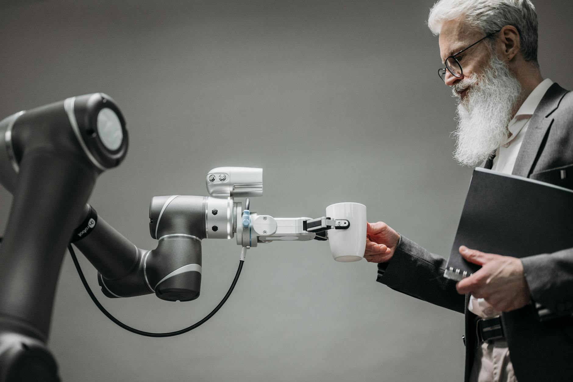 Starszy mężczyzna odbiera kubek od robota w nowoczesnym biurze